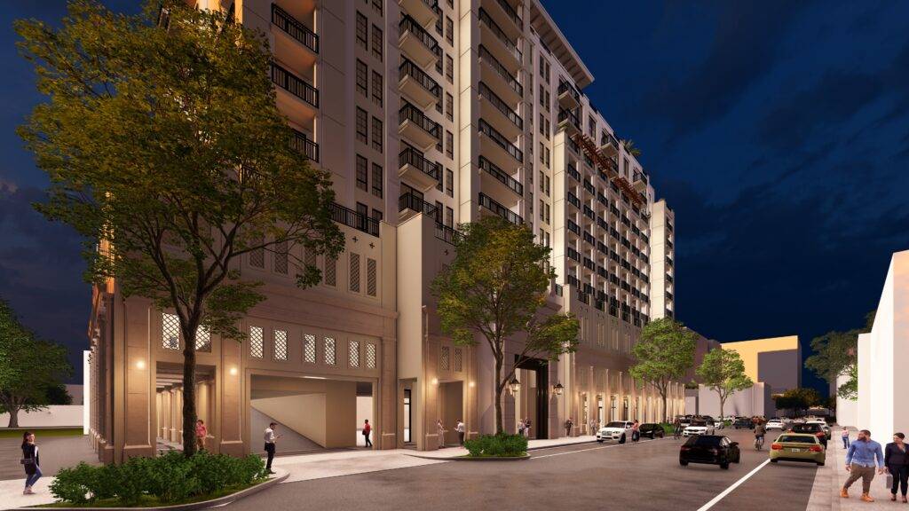 Urban street view at night with a modern, illuminated high-rise building and surrounding trees.