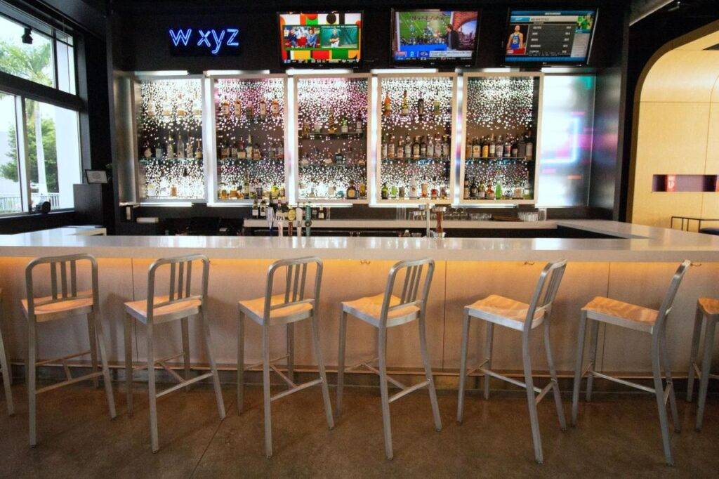 Modern bar interior with high chairs and illuminated shelves at Aloft Doral hotel.