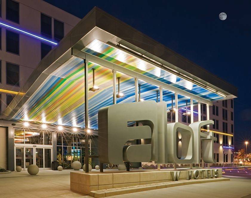 Night view of a modern hotel entrance with colorful illuminated awning and bold signage.