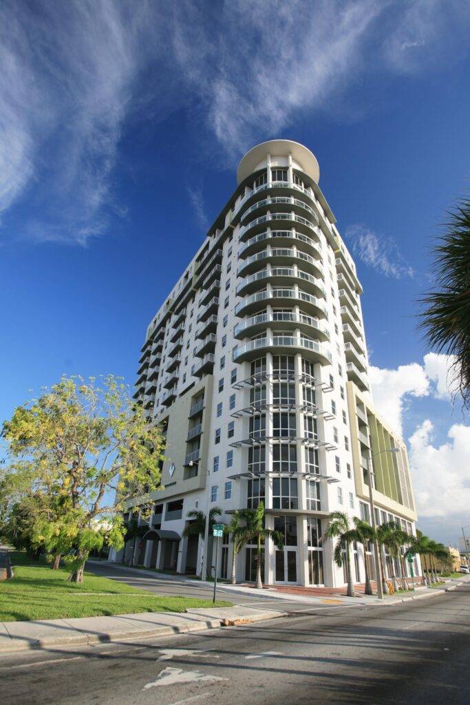 Modern high-rise building under a blue sky with lush greenery in an urban setting.