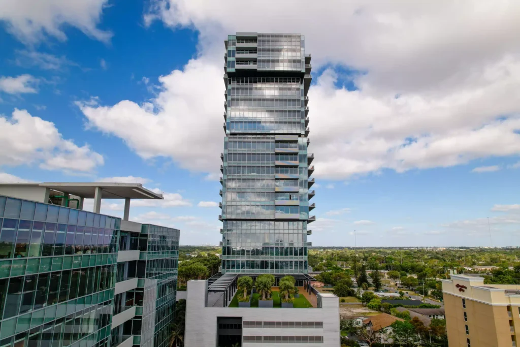 Modern glass skyscraper with a unique geometric design against a blue sky with clouds.