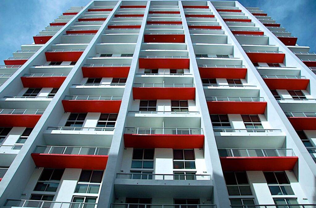 Modern high-rise building with striking red balconies against a blue sky backdrop.