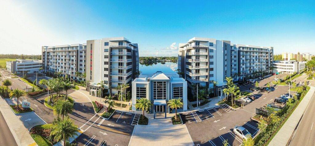 Modern waterfront apartment complex with palm-lined streets and blue skies.