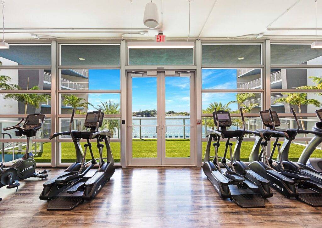Modern gym with treadmills facing a serene view of blue waters and palm trees.