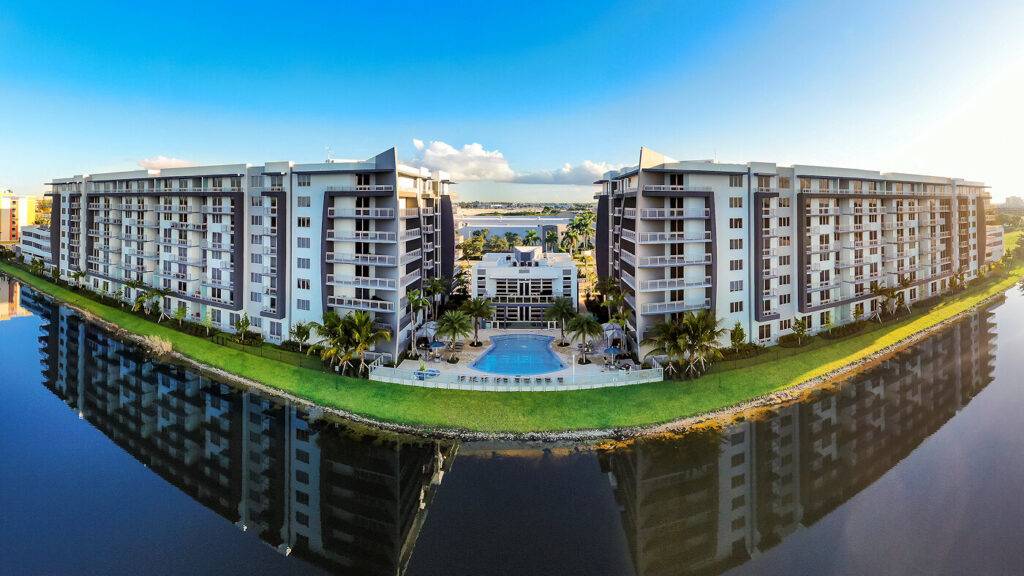 Panoramic view of luxury waterfront apartments with a reflecting blue sky and serene water.