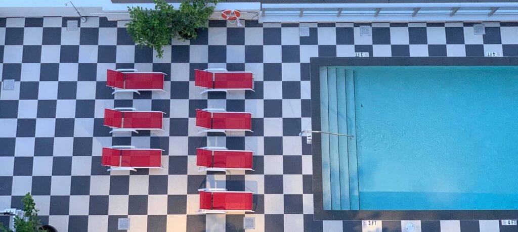 Aerial view of a poolside area with red lounge chairs on a black-and-white checkered floor next to a swimming pool.