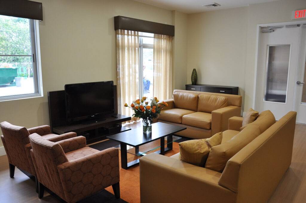 Modern living room with beige sofas, a flat-screen TV, and a coffee table with a vase of flowers.