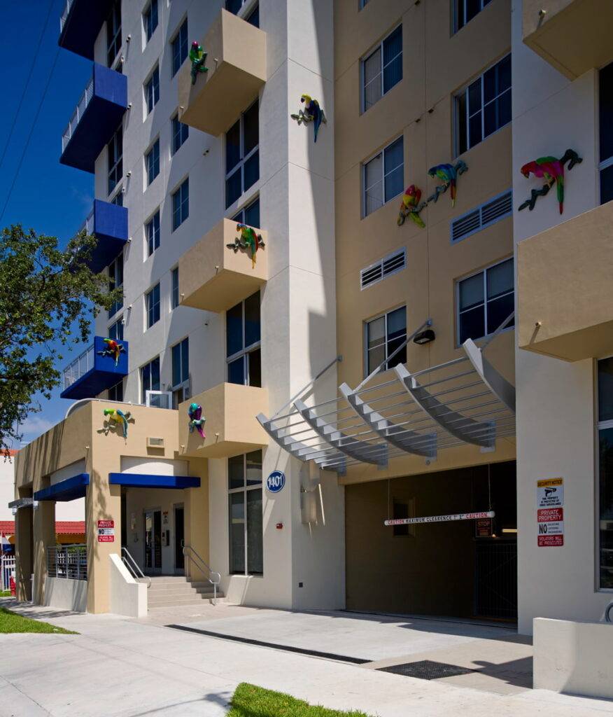 Colorful lizard sculptures on a modern beige building facade against a clear blue sky.