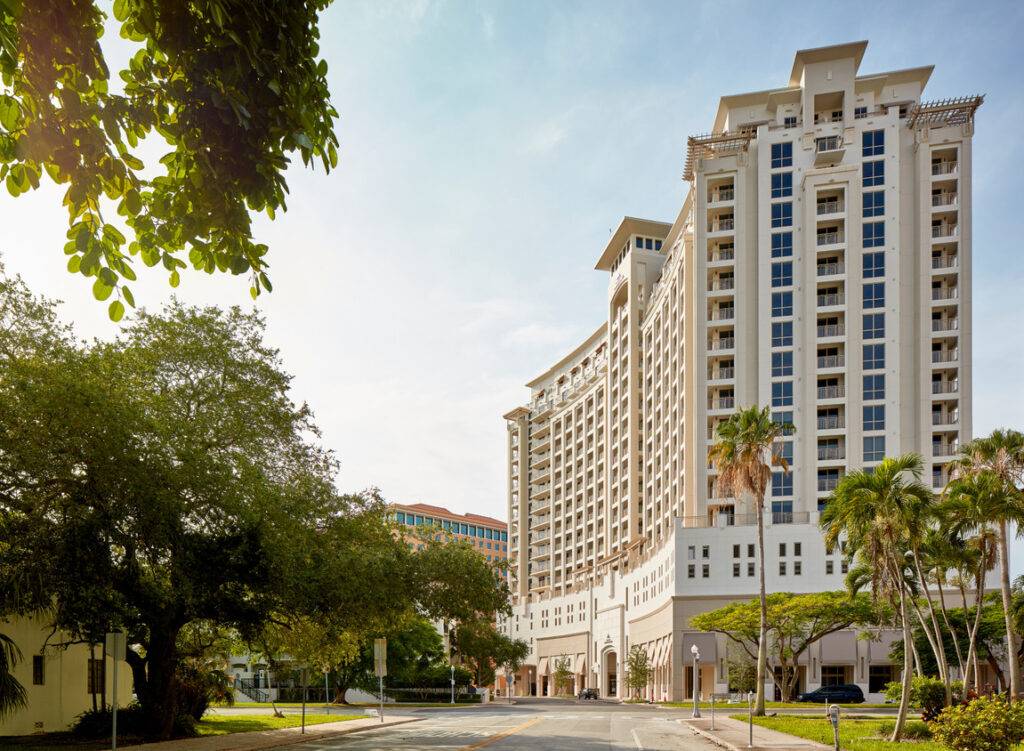 Modern high-rise building under a clear sky, framed by trees and urban surroundings.