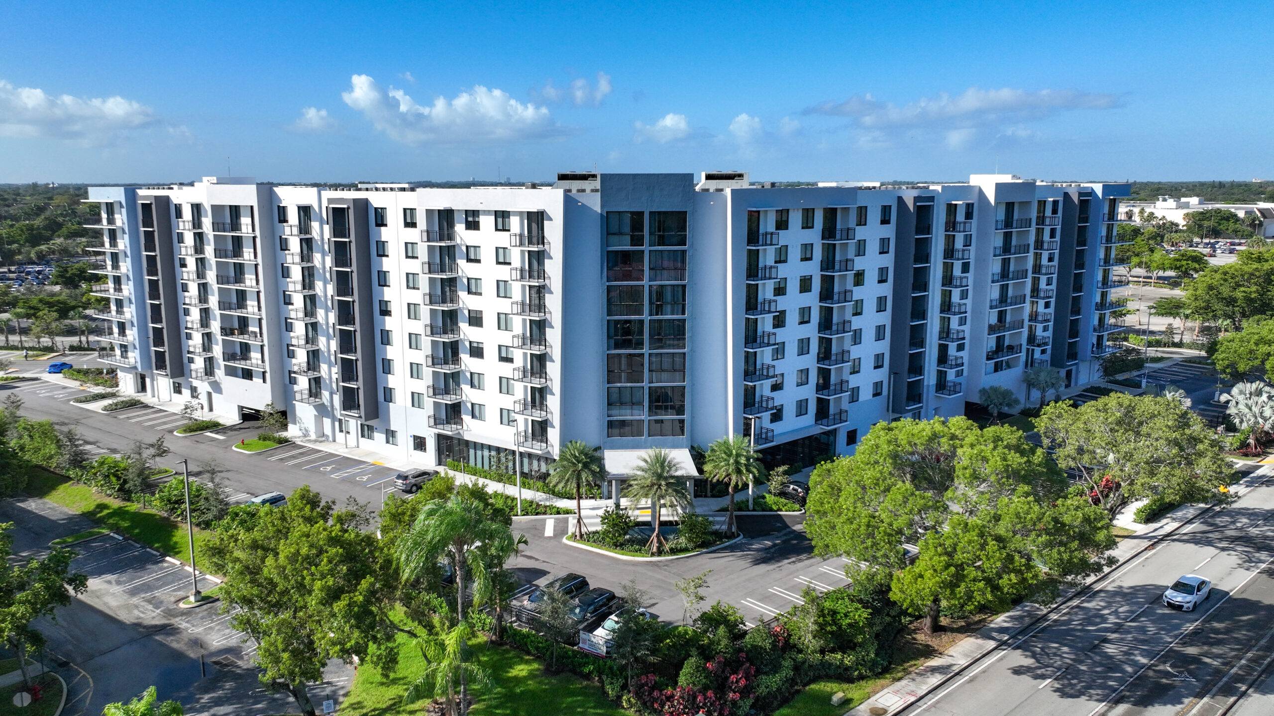 Aerial view of a modern multi-story apartment building surrounded by trees and clear skies.