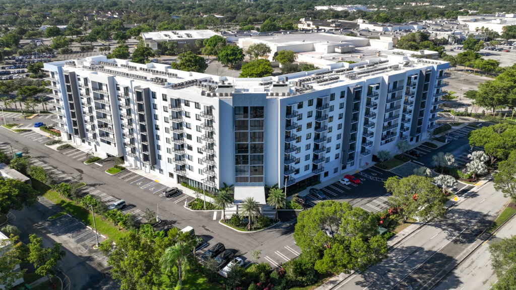 Aerial view of a modern multi-story apartment building surrounded by lush greenery and urban landscape.