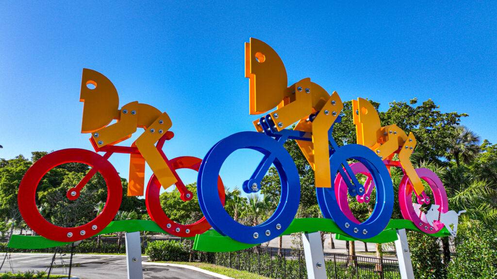 Colorful metal sculpture of cyclists against a bright blue sky.