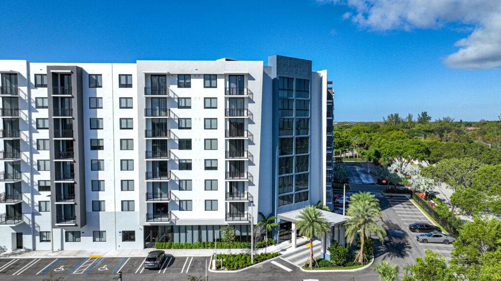Modern apartment building with balconies and palm trees in a sunny setting.