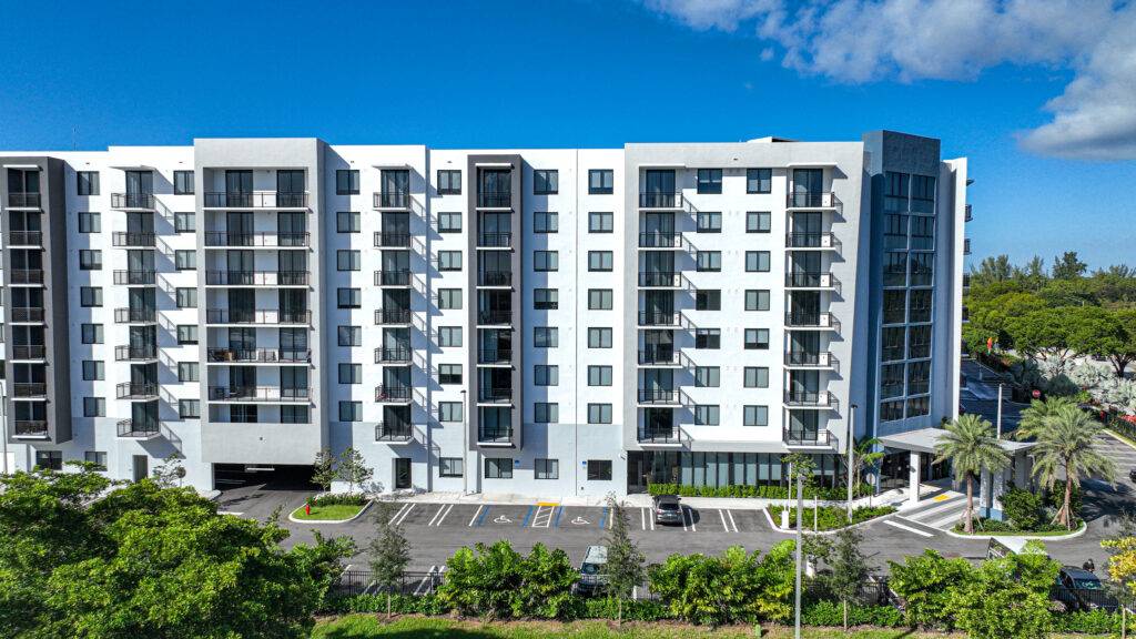 Modern white apartment building with balconies and lush greenery.