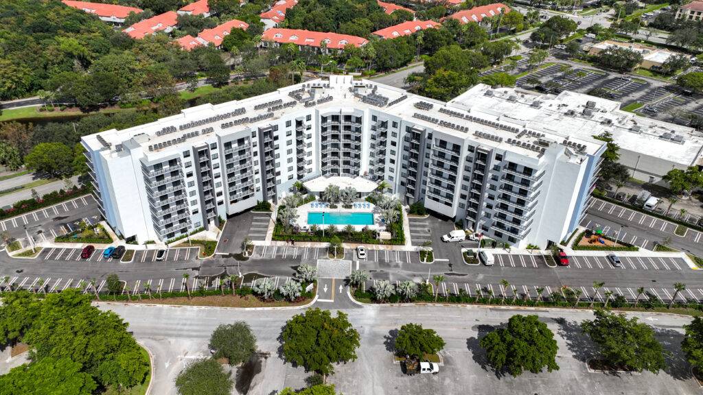 Aerial view of a modern residential complex with a central pool surrounded by lush greenery and parking areas.
