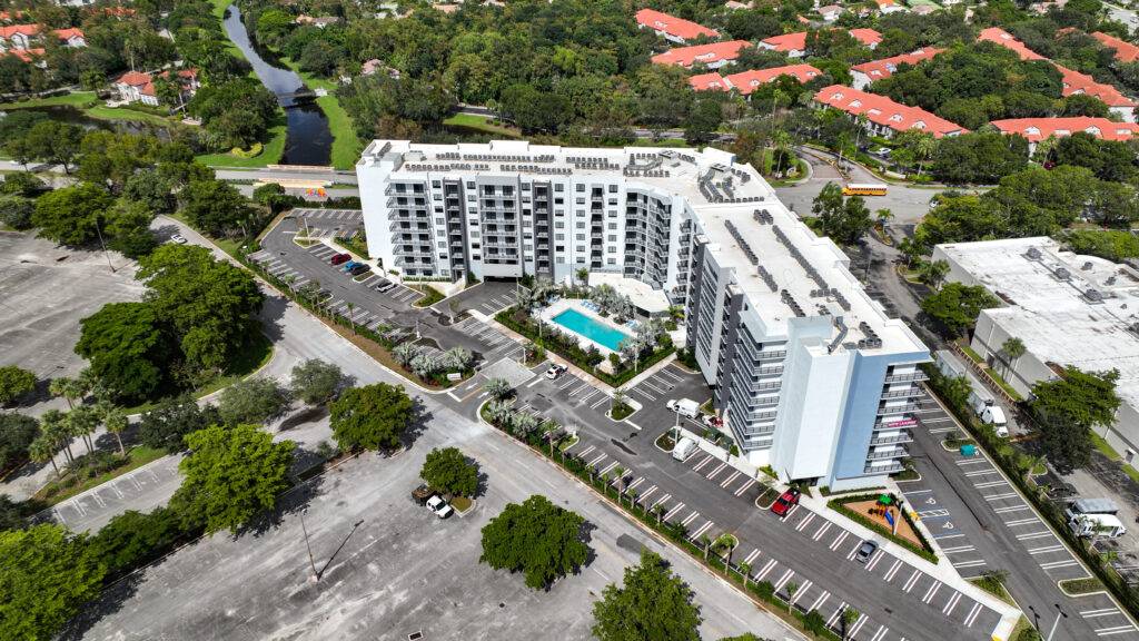 Aerial view of a modern residential complex with a central swimming pool surrounded by lush greenery and urban landscape.