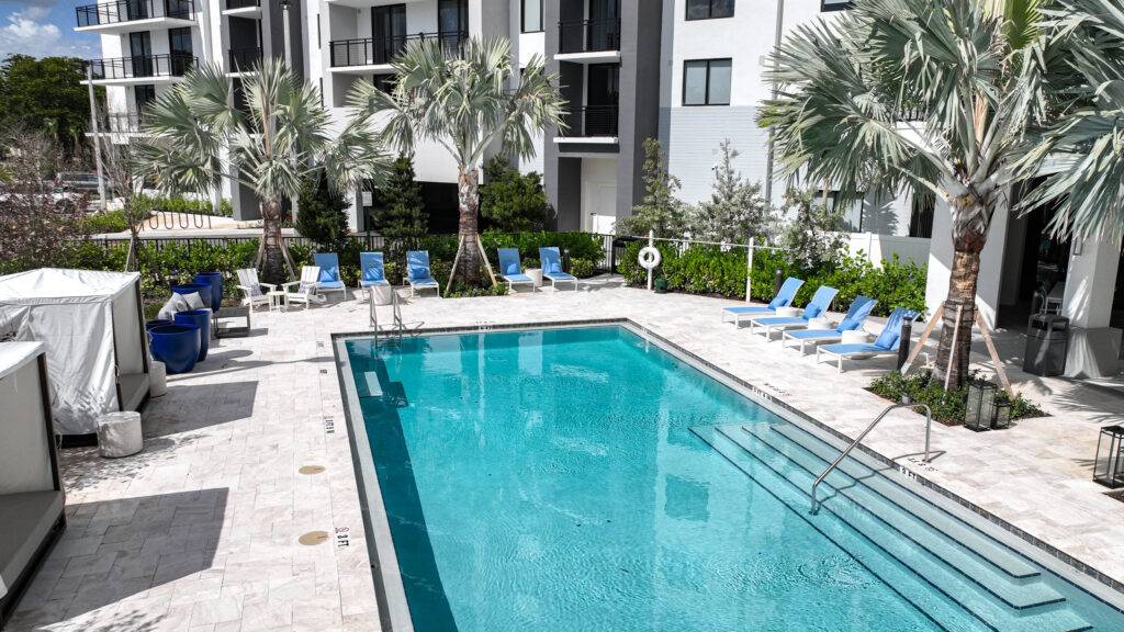 Modern outdoor pool with blue lounge chairs and palm trees.