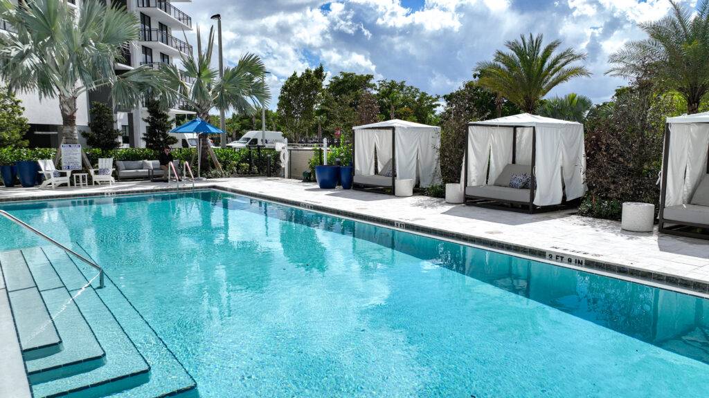 Luxurious poolside with cabanas and palm trees under a bright blue sky.