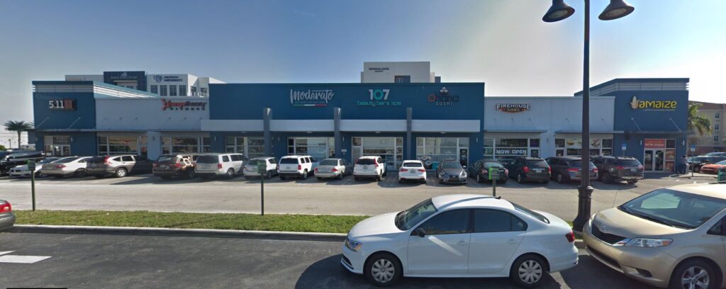 Modern retail center with multiple storefronts and a busy parking lot on a sunny day.