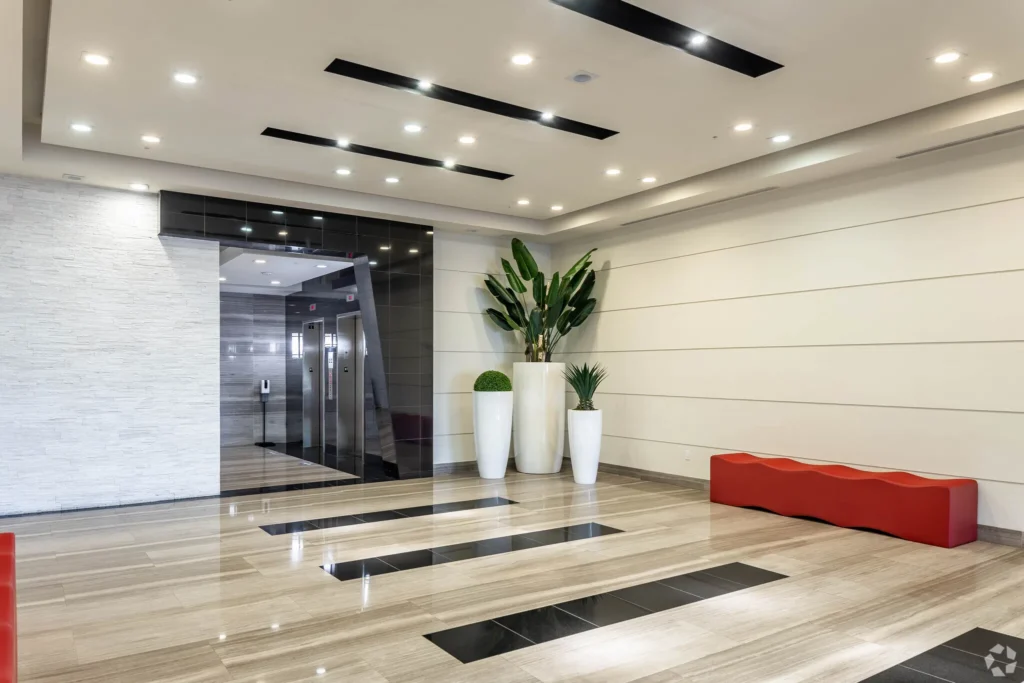 Modern lobby with sleek design, featuring a red bench, potted plants, and bright lighting.