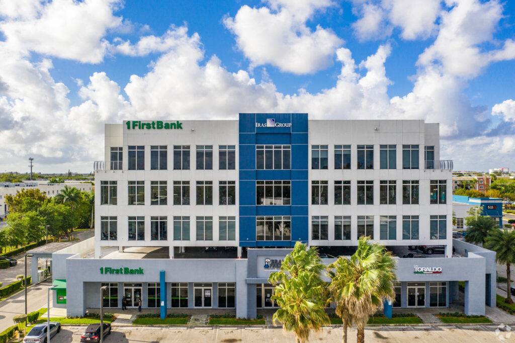 Modern office building with palm trees and blue sky background.