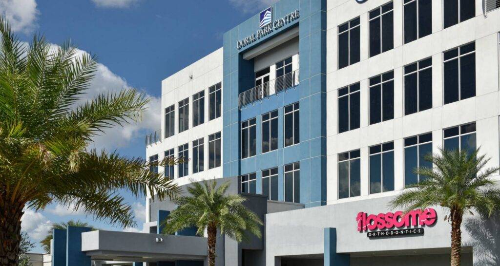 Modern office building in Doral Park Centre surrounded by palm trees under a bright blue sky.