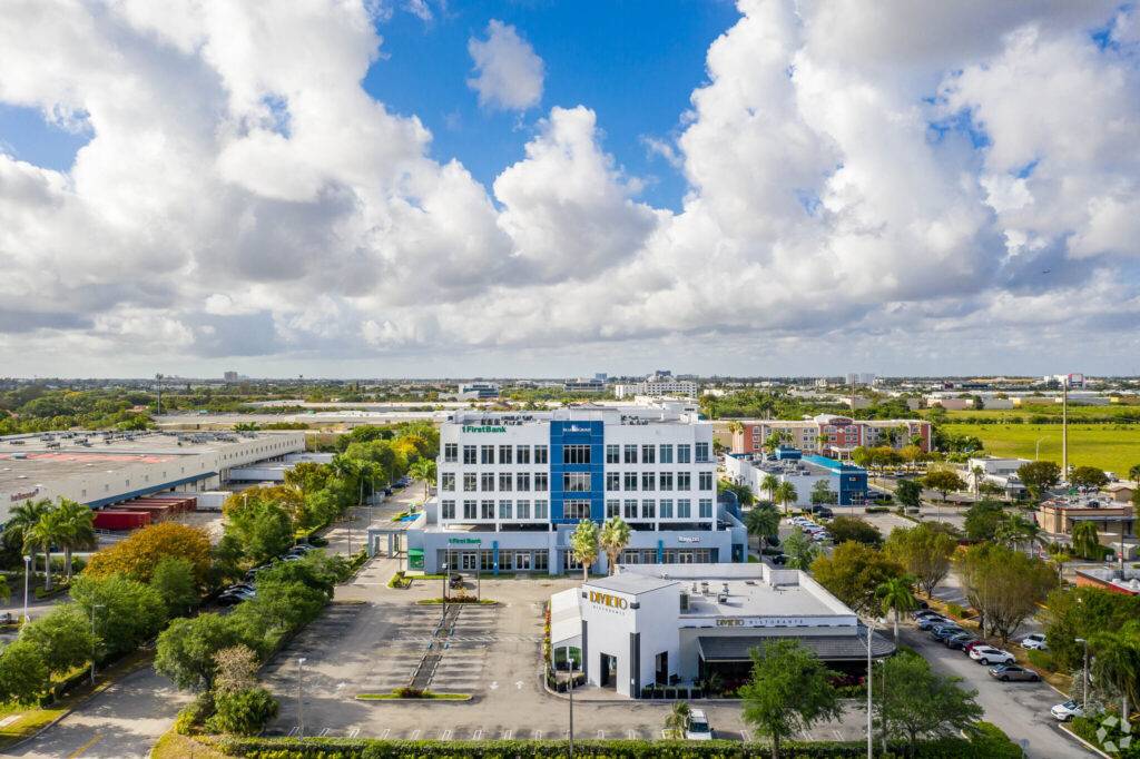 Aerial view of the modern Doral Park Centre surrounded by lush greenery and a vibrant urban landscape under a bright blue sky.