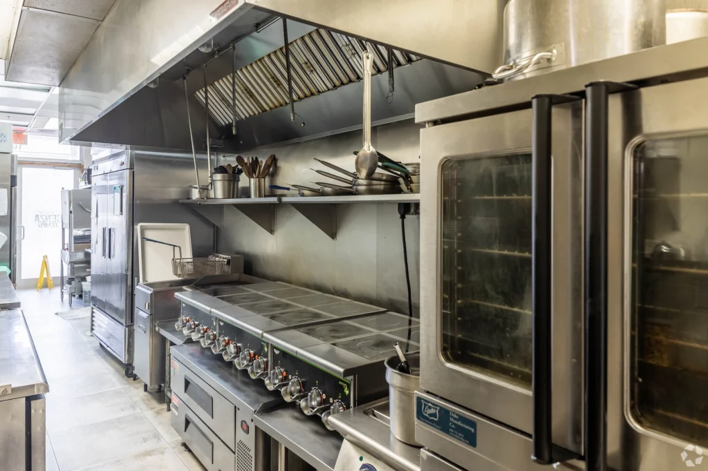 Commercial kitchen with stainless steel ovens and stovetops.