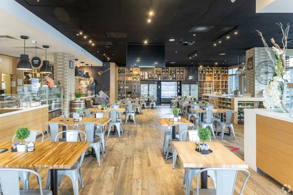 Spacious modern restaurant interior with wooden tables, metal chairs, and decorative shelves.