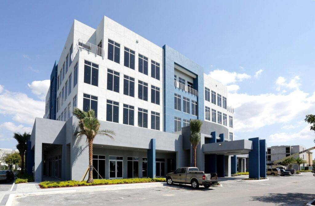 Modern office building with large windows and palm trees in front, under a clear blue sky.