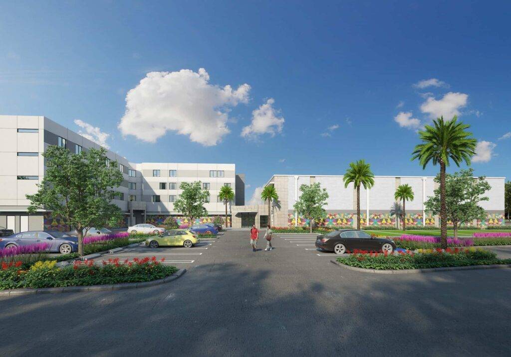 Modern residential complex with palm trees and colorful gardens under a clear blue sky.