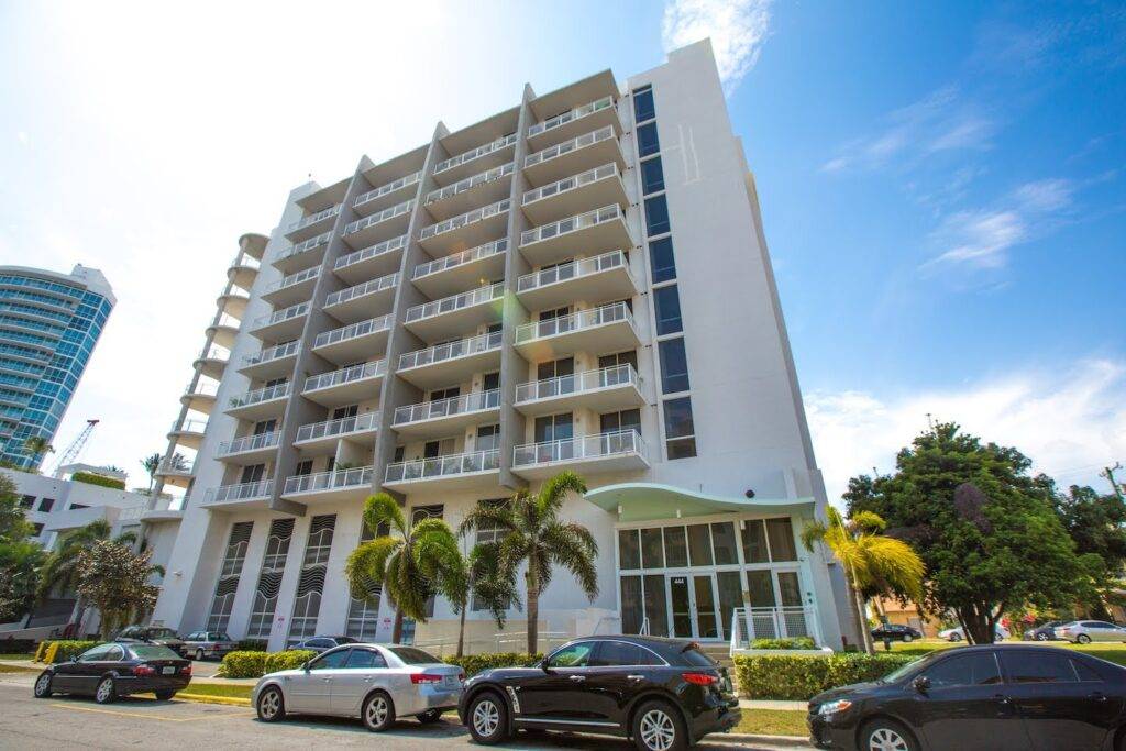 Modern high-rise building with palm trees and parked cars in a sunny urban setting