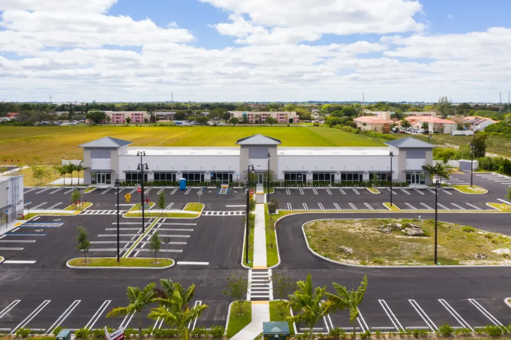 Modern commercial building surrounded by palm trees with an empty parking lot under a sunny sky.