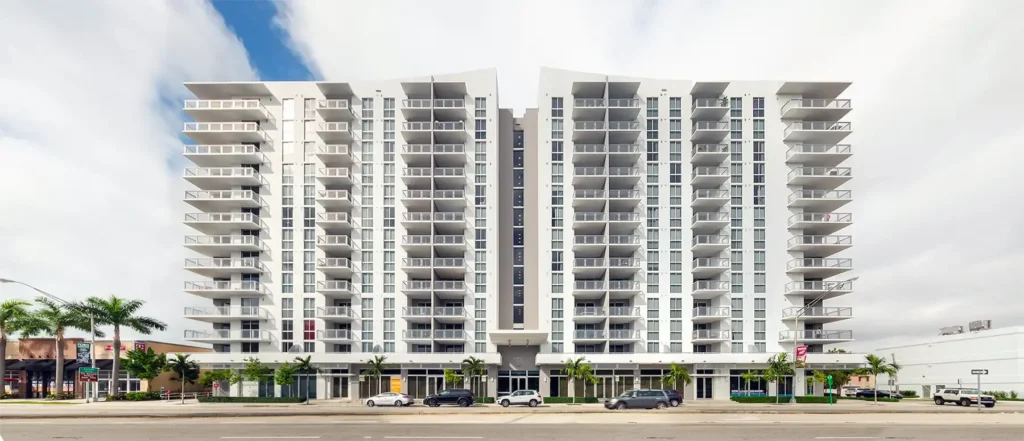 Modern high-rise apartment building with white facade and balconies under a partly cloudy sky.