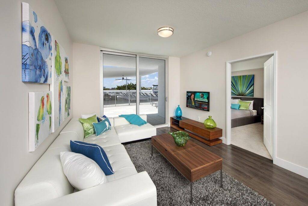Modern living room with white sofas, colorful art, and a balcony view in a contemporary apartment.