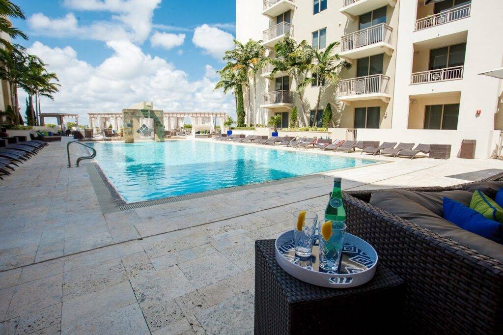 Luxurious apartment building with a stunning pool area and poolside seating under a bright blue sky.