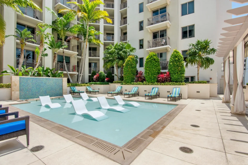 Luxurious outdoor pool area with lounge chairs at a modern apartment complex surrounded by lush greenery.