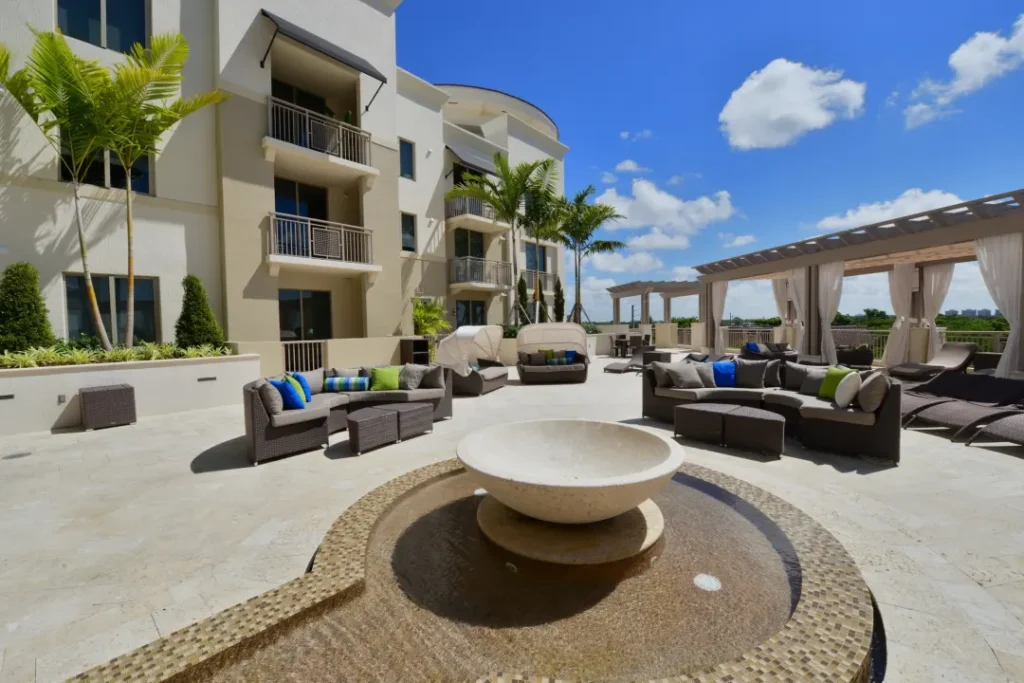 Modern apartment building with luxury outdoor seating and water feature under a blue sky.