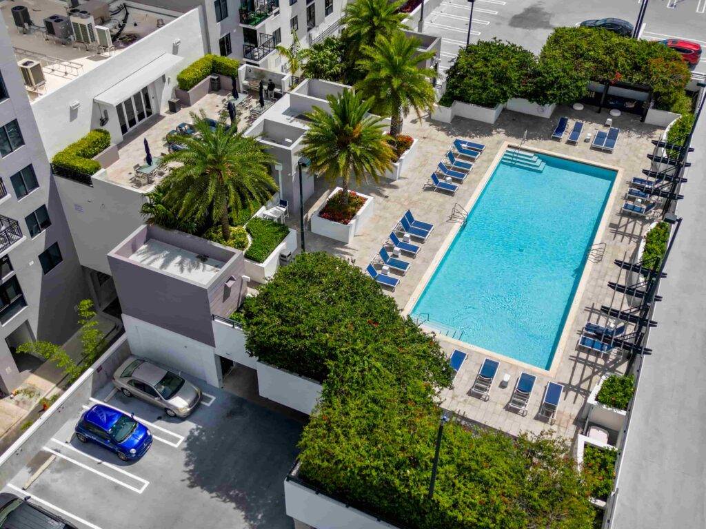 Aerial view of a modern apartment complex with a central pool surrounded by lush greenery and lounge chairs.