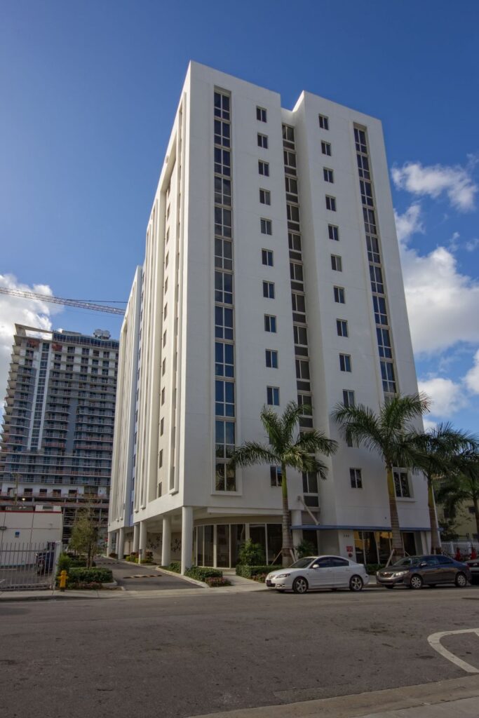 Tall modern apartment building with palm trees under a blue sky.