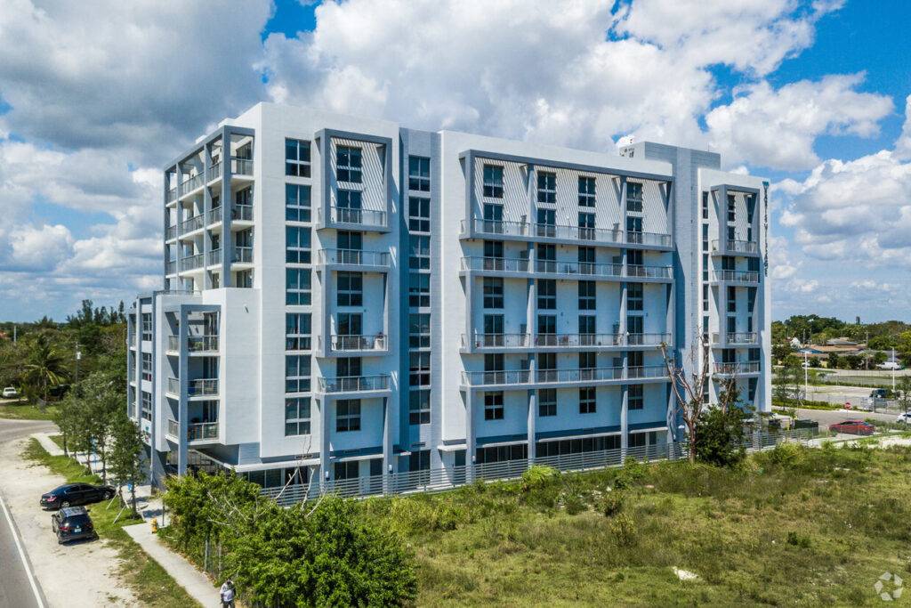 Modern residential building under a blue sky with surrounding greenery.