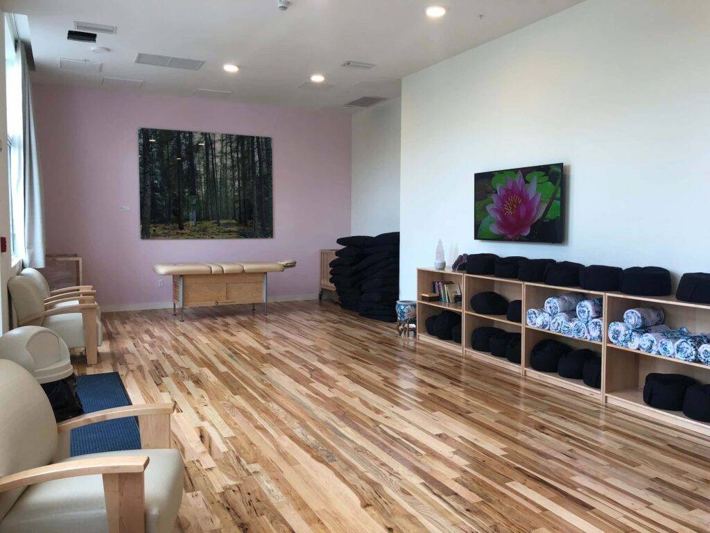 Yoga studio with wooden floors, chairs, paintings, and shelves of yoga mats and blankets.