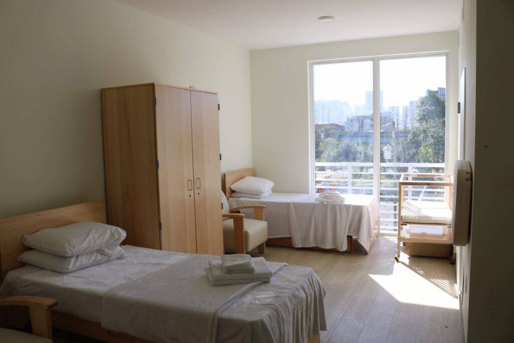 Sunny bedroom with two neatly made beds, wooden furniture, and a large window.