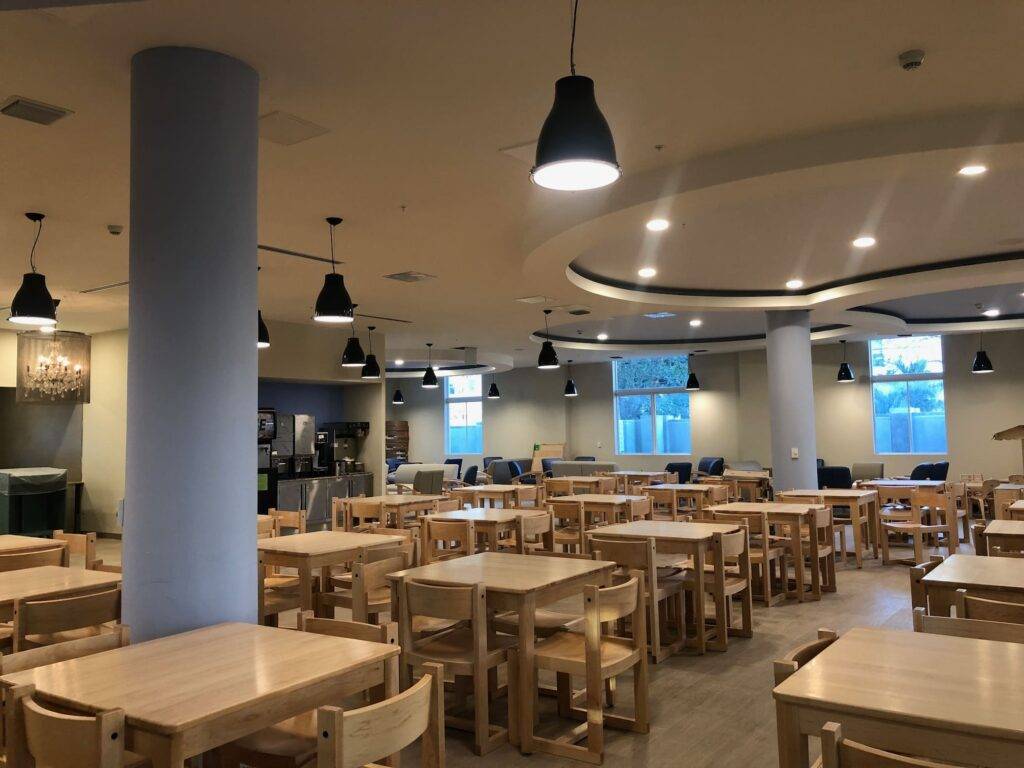 Spacious dining area with wooden tables and chairs, modern lighting, and large windows.
