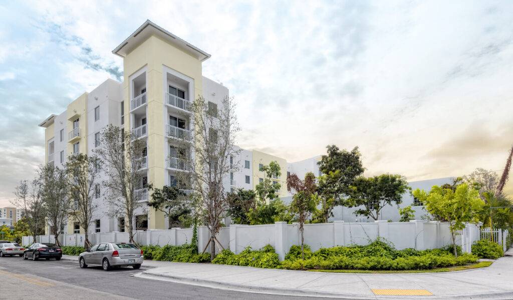 Modern residential building with lush greenery and parked cars in a serene neighborhood setting.