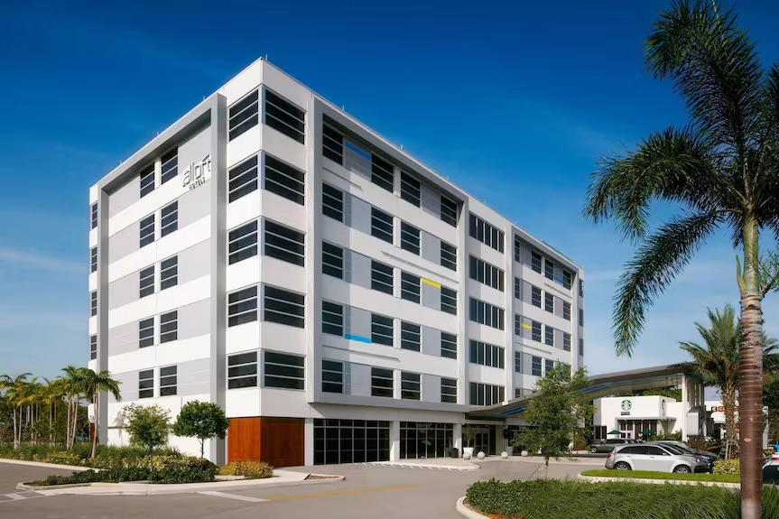Modern office building with palm trees and a clear blue sky.