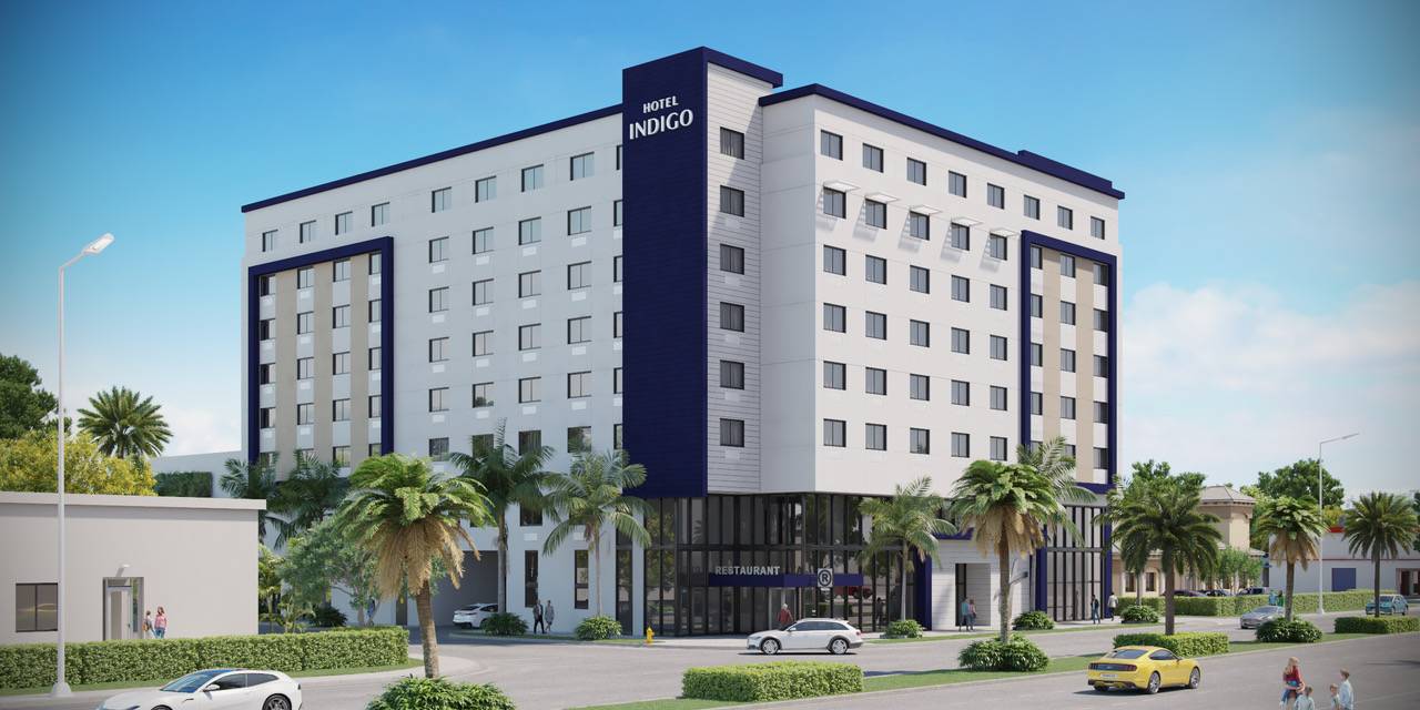 Modern hotel building with palm trees and cars in front, set against a clear blue sky.