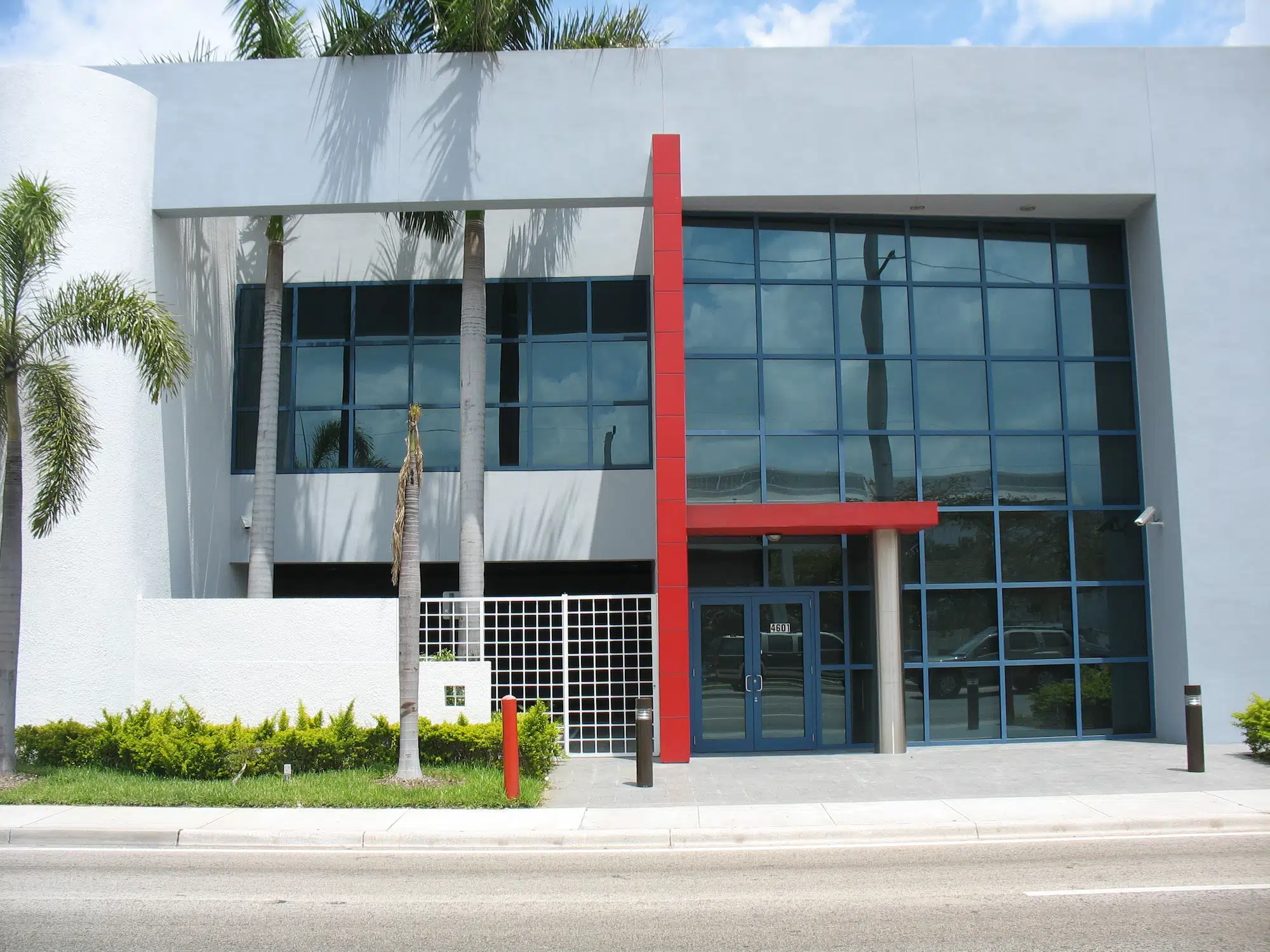 Modern commercial building with large glass windows and a bold red accent feature, set against a clear sky.