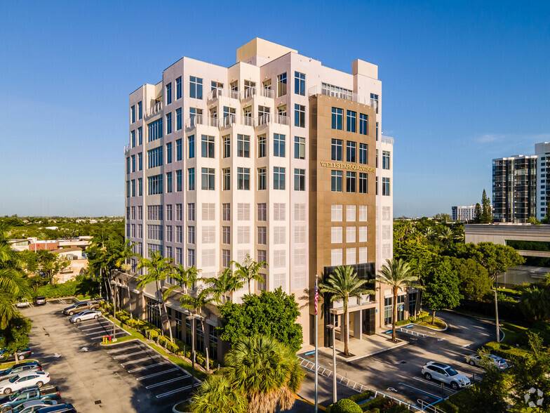 Aerial view of a modern multi-story office building surrounded by palm trees on a sunny day.