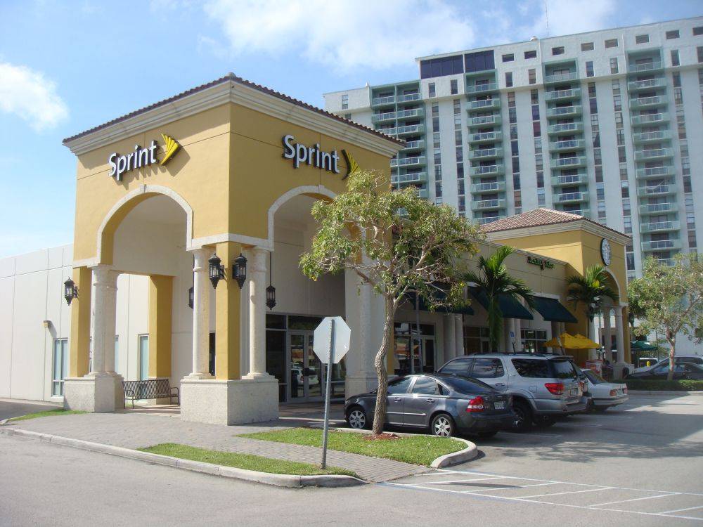 A Sprint store in a modern yellow building with arches, located in a bustling city area with high-rise apartments in the background.